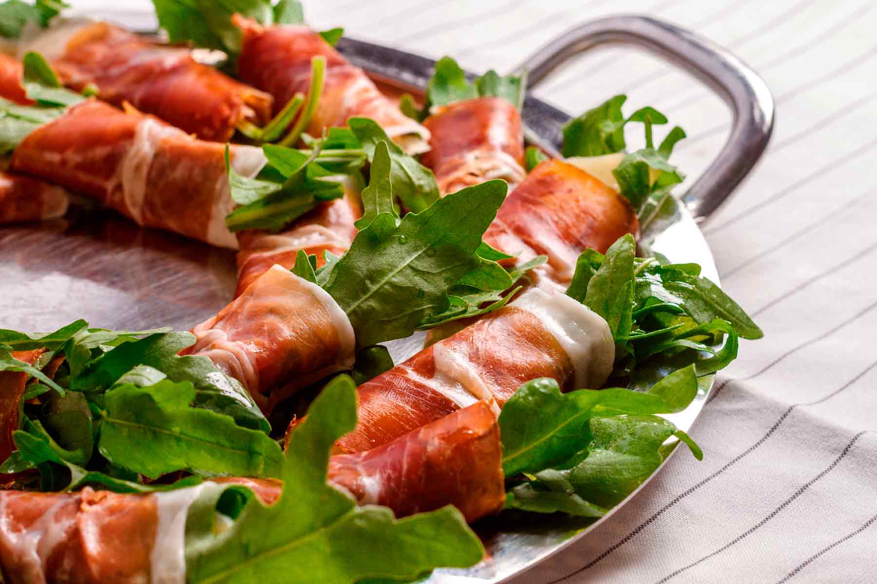 Rollitos de jamón ibérico con rúcula sobre bandeja 